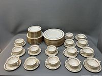 Full display of Lenox Golden Wreath dinnerware set with plates stacked and cups/saucers arranged around them.