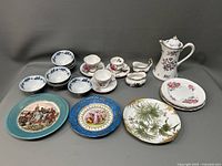 Full lot showing assorted small bowls, plates, teapot, creamer, sugar bowl, cups and saucers arranged on grey backdrop.