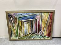 Front view of mixed-media abstract painting with attached glass and light wood frame against white wall.