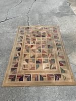 Full view of the rectangular rug placed on concrete, showing the beige base and multicolored geometric block pattern with a framing border.