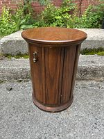 Front and side views of a vintage cylindrical wooden end table with cabinet door and a small round metal handle showing wood grain and light surface wear.