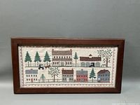 Frontal photo of the framed needlepoint folk art sample showing the entire village scene.