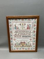 Full view of framed needlepoint sampler showing complete design and wooden frame