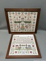 Two framed needlepoint samplers leaning against a gray background, showing full pieces and frames.