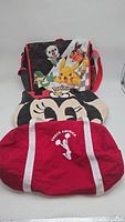 Three bags displayed: Pokémon messenger bag, Mickey Mouse tote, and red Cheer America duffel bag.