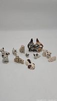 12 multicolor dog-themed figurines made of ceramic, chalkware, and porcelain, arranged on white background