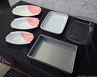 Set of five dishes including three ceramic serving plates with pink and cream, floral trimmed rectangular casserole dish, clear glass baking dish, and ribbed metal baking pan.