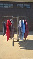 Seven men's clothing items hanging on a rack. Visible are shirts and hoodies in various colors including red, blue, and plaid patterns.