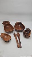 Full view of two large pineapple-shaped wooden serving bowls, six small matching bowls, and three wooden serving utensils with carved details and wood grain visible.