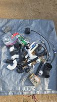 Overview of various plumbing parts spread on a blue tarp, including black and white plastic pipes, connectors, metal braided hoses, and small fittings.