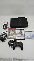 Full bundle showing the PS2 console, aftermarket controller, two game cases (Grand Theft Auto and Madden 06), PlayStation 2 camera, online startup disc, and power cable.