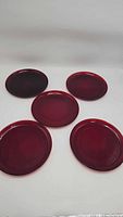 Five vintage red glass plates arranged on a white background, showing the deep red color and smooth glass surface.