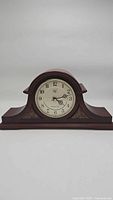 Full frontal image of mantel clock showing wood construction, shape, and base details.