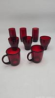Front view of 8 red glass drinkware pieces including mugs and glasses arranged in two rows