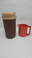 Side view of two items: a large brown thermos with beige lid and a bright orange plastic pitcher with handle