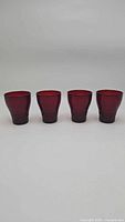 Set of four vintage ruby red drinking glasses lined up in a row, showing their overall shape and color.