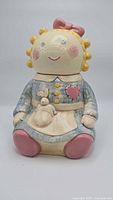 Front view of the ceramic ragdoll cookie jar showing painted face, blue dress, pink shoes, and bunny detail