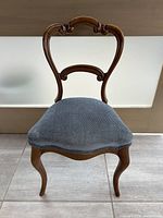 Front view of antique balloon back chair showing carved wooden frame and blue corduroy seat upholstery