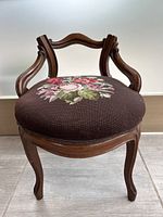 Front view of antique needlepoint floral vanity chair showing seat upholstery and wooden frame.