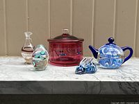 Full lot view showing all six art glass pieces side by side on stone surface against neutral background.