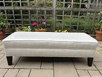 Front view of bench outdoors against wooden trellis and potted plants