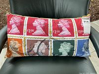 Photo of rectangular decorative pillow with colorful British postage stamp pattern, showing front side with Queen Elizabeth II profiles in various colors and denominations.
