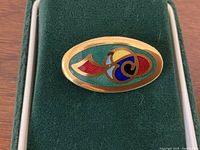 Oval brooch showing colorful Celtic enamel design on gold-tone metal.