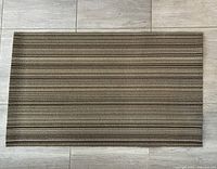 Full view of the rectangular striped rug laid flat on tile floor, showing horizontal stripes in multiple shades of brown and beige.