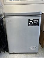 Silver grey Danby chest freezer showing front facade with logo, control dial, and energy guarantee sticker.