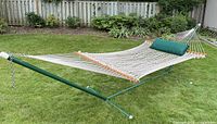 Double hammock set up on grass, showing green metal frame, white woven rope hammock, and green cushion.