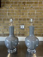 Front view of two grey ceramic table lamps on clear lucite bases with chrome hardware, no shades