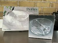 Two boxed glass serving sets, one a chip and dip platter from Profiles The Versatiles Collection, and one a divided glass bowl with serving tongs from the Safari line.