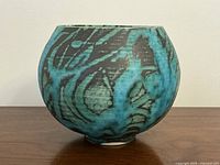 Front view of round turquoise and black glazed porcelain vase on wooden surface