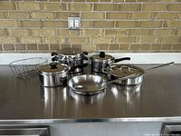 Overall view of six-piece cookware set on stainless steel surface against brick wall