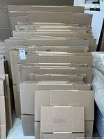 Large stacks of folded cardboard boxes of various sizes arranged in bundles, leaning against a wall.