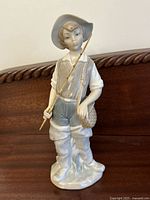 Front angle view of the Lladro porcelain boy fishing figurine showing details of face, clothing, fishing pole, and basket.