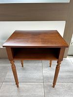 Front view of the solid maple wood end table showing the open storage shelf and carved legs.