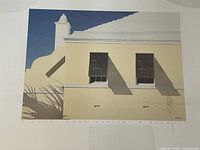 Close-up of signed print showing a pale yellow building under a blue sky with shadows and architectural details