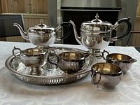 Full view of the silver plated tea set with teapot, hot water pot, creamer, sugar bowl, two small bowls, and round tray