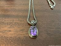Close-up of the amethyst pendant showing cushion-cut stone and detailed silver mounting with floral designs.