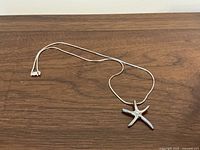 Full length view of the sterling silver starfish necklace laid flat on a wooden surface, showing the chain and pendant.