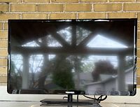 Front view of Toshiba 32-inch flat screen TV on stand, screen reflective with background visible