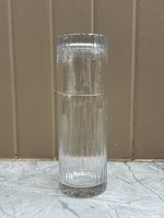 Clear vintage glass bedside carafe with textured vertical lines, standing alone against a neutral background.