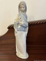 Full view of the vintage Lladro porcelain figurine showing the veiled lady holding a bouquet of calla lilies, posed on a wooden surface.