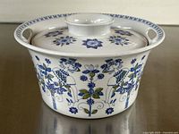 Front side view of ceramic lidded casserole dish showing detailed blue and green floral and stylized human figure pattern