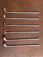 Six silver plated golf club drink stir sticks laid out showing full length and variety of club heads.