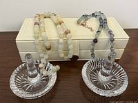 Image showing two Waterford crystal ring holders placed on a cream leather jewelry box, along with two beaded necklaces draped over the box.