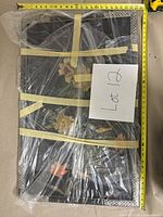 Framed artwork wrapped in plastic with visible 3D flower elements, taped for protection, with a measuring tape showing width around 26 inches.