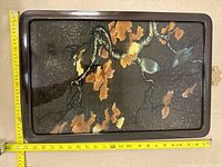 Top view of framed glass panel artwork featuring birds on branches with autumn leaves. A tape measure is placed on the left side and bottom edge of the frame to show dimensions.