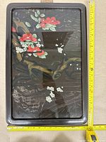 Front view of framed floral artwork showing scratches and wear on the black wood frame, with several red flowers depicted on artwork.